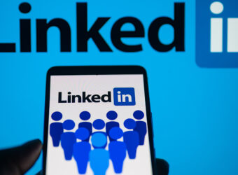 LinkedIn logo displayed on a smartphone with LinkedIn on screen seen in the background, in this photo illustration.